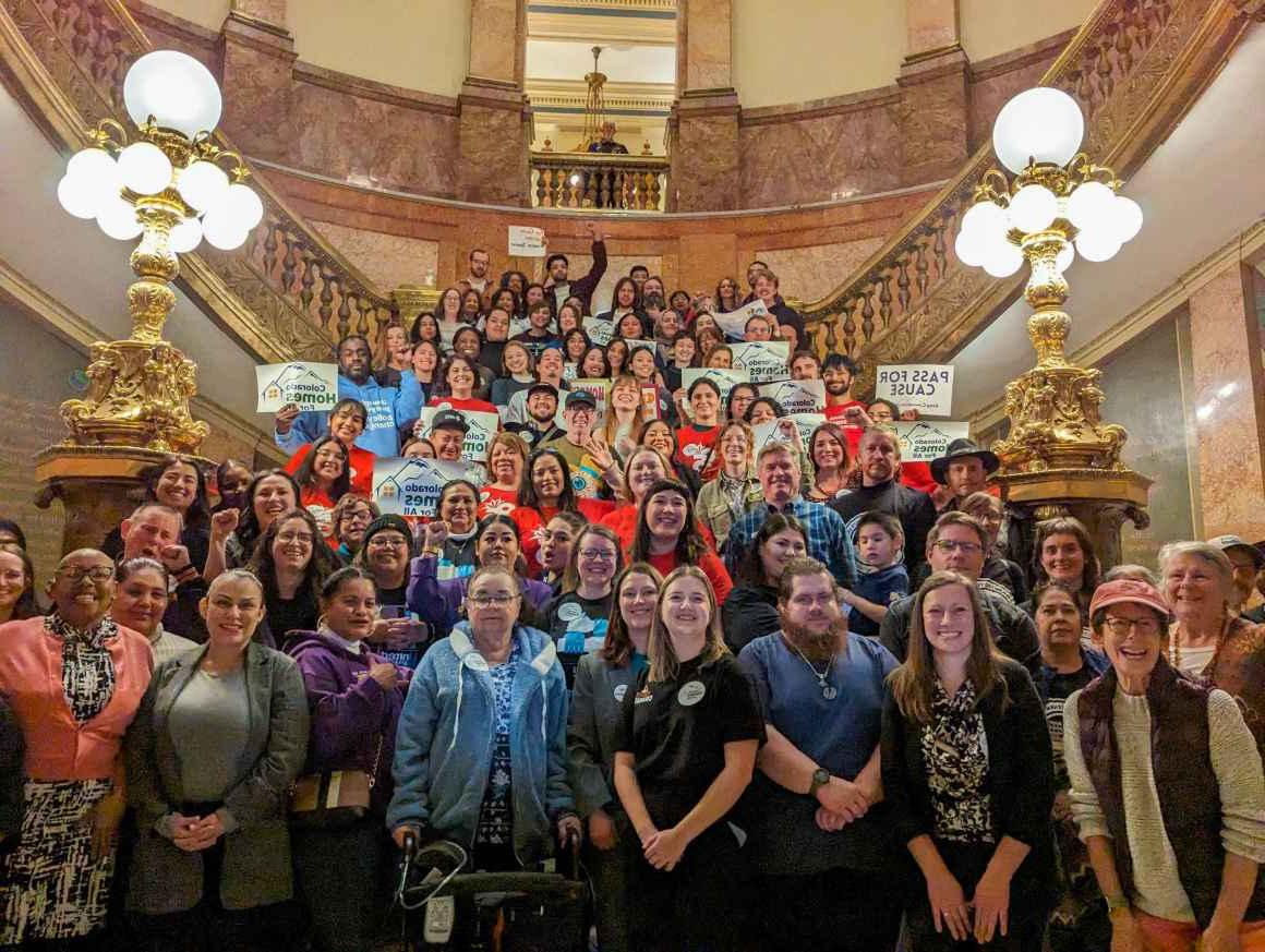 Photo of a crowd of people standing on the stairs of the Colorado state capitol rotunda and holding up signs